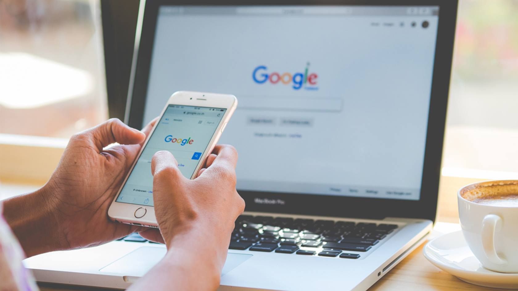 Laptop mit Google-Startseite im Hintergrund, zwei Handy mit Handy und Google-Startseite im Vordergrund