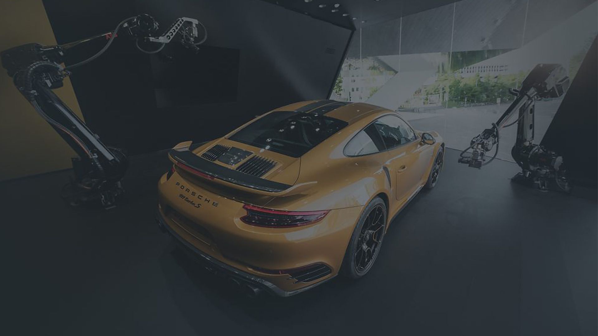 Ein goldener Porsche 911 Turbo S Exclusive steht in einem Raum und wird von zwei Roboterarmen gefilmt.