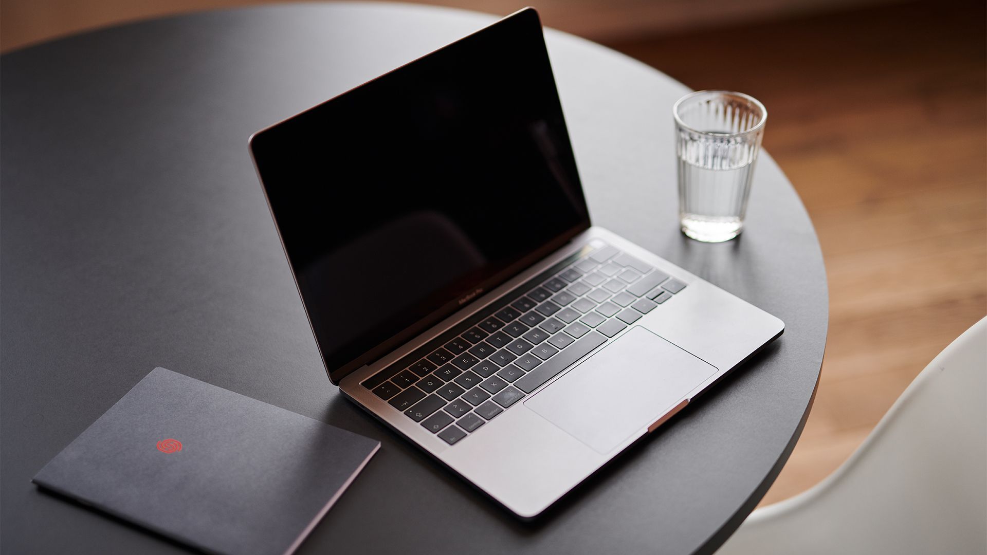 Laptop mit Notizheft und Wasserglas