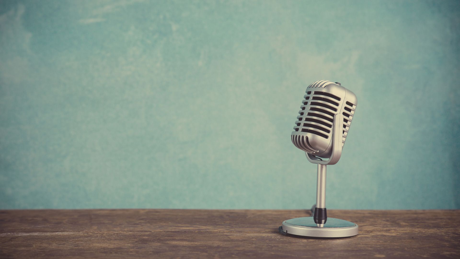 Oldschool Mikrofon auf einem Holztisch vor blauen Hintergrund.