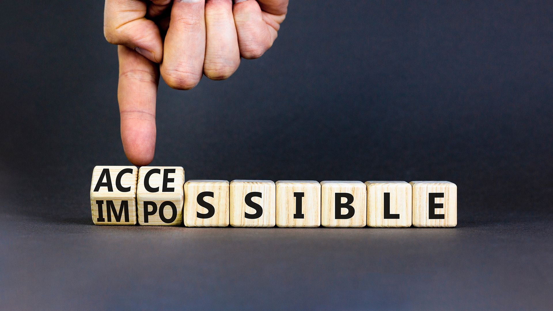 The finger of one hand turns wooden cubes with letters that form the word “IMPOSSIBLE” into “ACCESSIBLE”.